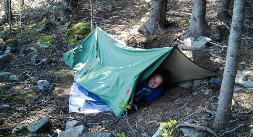 a person smiles while laying under a tarp in the woods on an outward bound expedition 